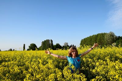 Full length of happy young woman with arms raised on field against sky
