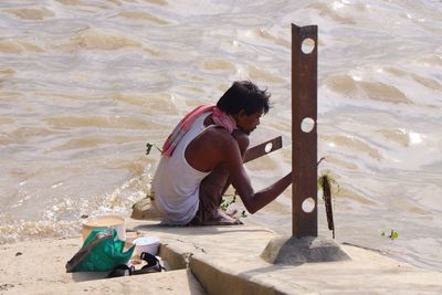 Full length of young man holding sunglasses at beach