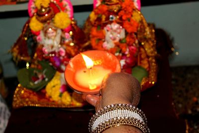 Cropped hand of woman praying with lit diya at home