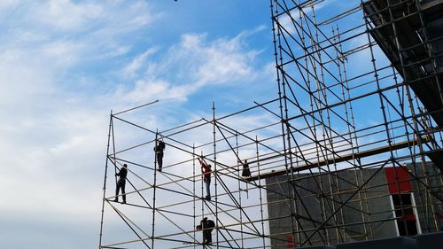Low angle view of manual workers on scaffoldings against sky