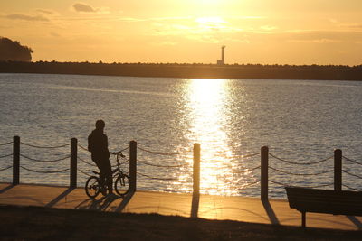 Silhouette man with bicycle on railing against sky during sunset