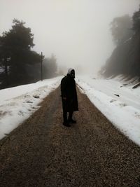 Full length of man wearing warm clothing while standing amidst road by snow during foggy weather