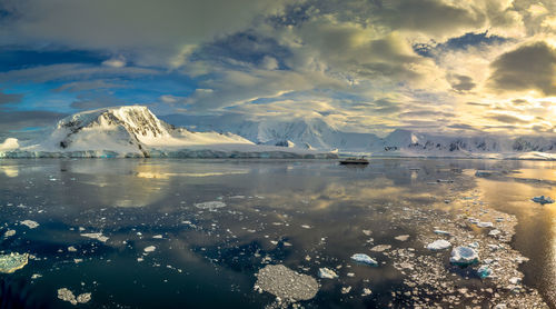 Scenic view of sea by snowcapped mountains against sky