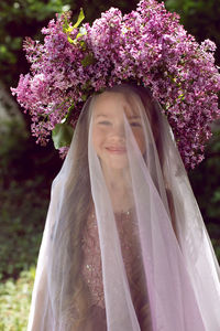 Caucasian girl child seven years old in a purple dress stands in nature with a wreath of lilacs