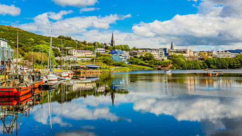 Pier in clifden port at high tide, moored boats, water mirror reflection, townscape against sky