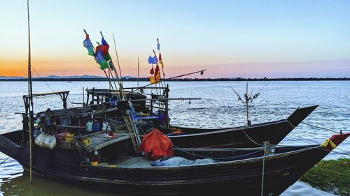 Fishing boats moored in sea at sunset