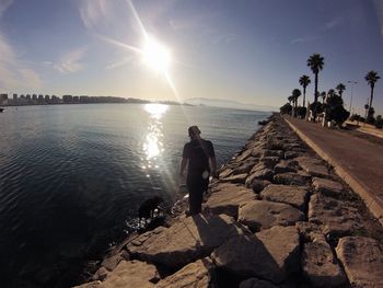 Rear view of man on sea against sky during sunset