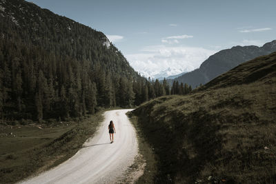 Woman walking on dirt road against sky