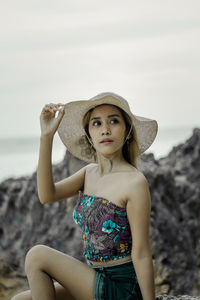 Portrait of beautiful young woman sunbathing wearing hat against sky