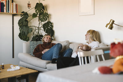 Smiling mothers relaxing on sofa with newborn baby