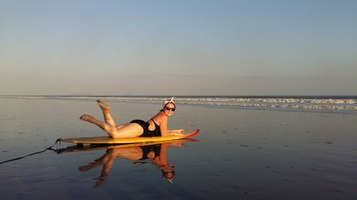 Portrait of smiling young woman in bikini lying on surfboard at beach