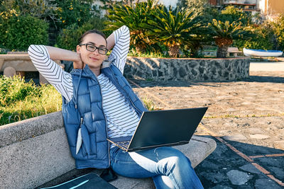 Beautiful sporty woman with laptop computer working outdoors while sitting on bench at the seaside. 