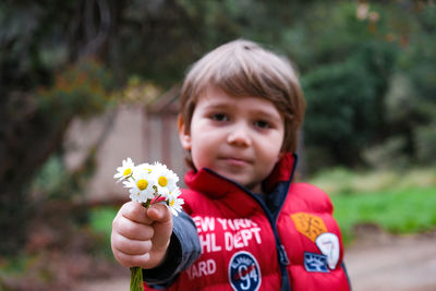 Portrait of boy holding flower against blurred background