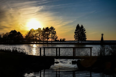 Silhouette plants by lake against sky during sunset