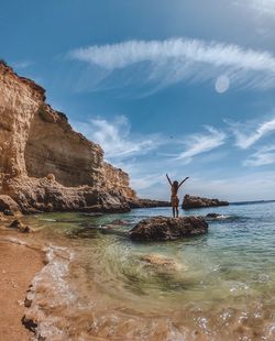 Man standing on rock by sea against sky