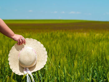 Cropped hand of woman holding hat on field