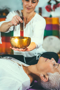 Midsection of woman playing singing bowl for customer in spa