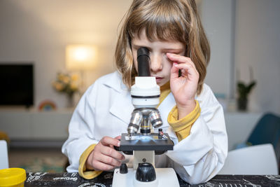 Girl in lab coat looking through microscope at home