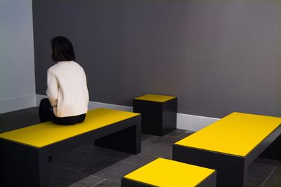 Rear view of woman sitting against yellow wall