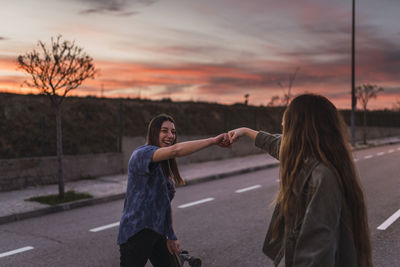 Cheerful female friends punching fists on road