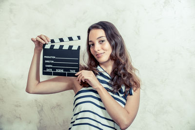 Portrait of young woman holding film slate by wall