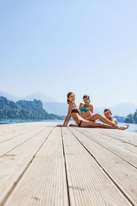 Portrait of happy friends sitting on pier over lake