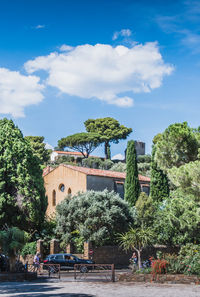 People sitting by trees and building against sky