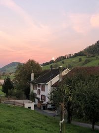 Trees and houses on field against sky during sunset