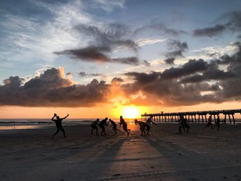 People playing on sand against sea during sunset