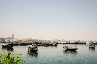 Boats moored in river by buildings against clear sky