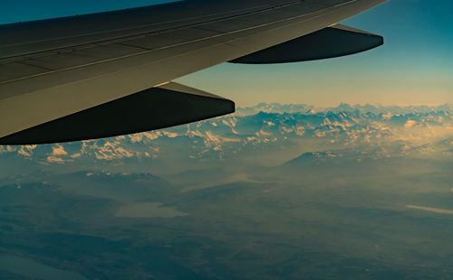 Wing of plane over mountain cover with white snow. airplane flying on blue sky. scenic view.