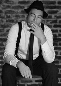 Young man smoking cigarette against brick wall