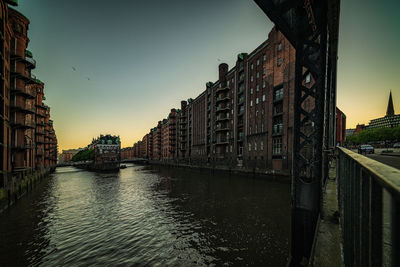 Bridge over river amidst buildings against sky at sunset