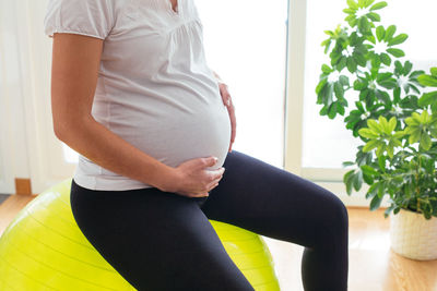 Midsection of woman with arms raised standing against wall