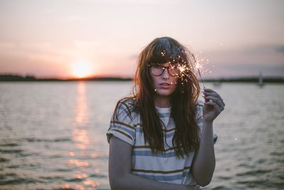 Portrait of young woman wearing sunglasses against sea during sunset