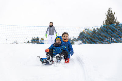 Full length of siblings tobogganing on snow during winter