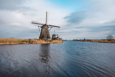 Traditional windmill by lake against sky