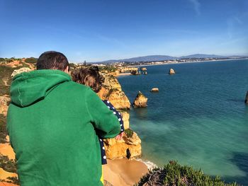 Rear view of father with daughter at praia do camilo against sky