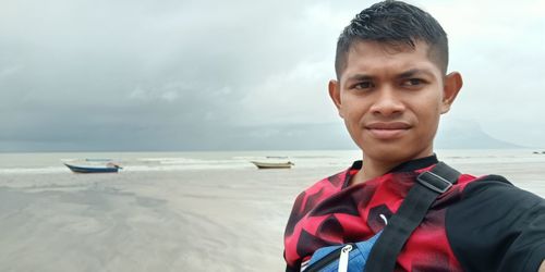 Portrait of boy standing on beach against sky