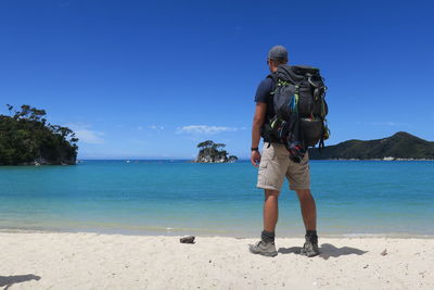 Full length of man standing at beach against blue sky