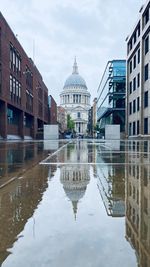 Street level view of saint pauls cathedral framed between modern buildings. reflections wet pavement