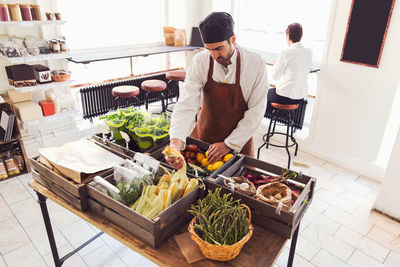 High angle view of male owner arranging vegetables at grocery store