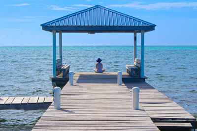 Rear view of woman sitting on pier at sea against sky