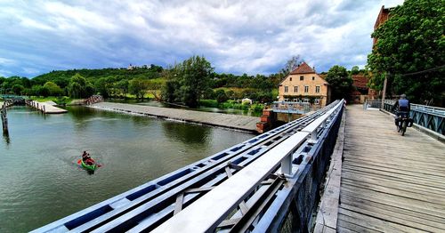 Footbridge over river amidst buildings against sky