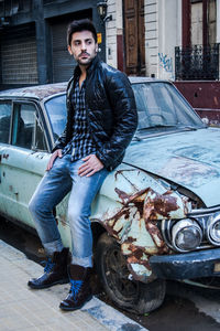 Thoughtful young man looking away while sitting on abandoned car