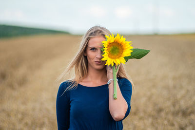 Beautiful young woman holding sunflower while standing on field