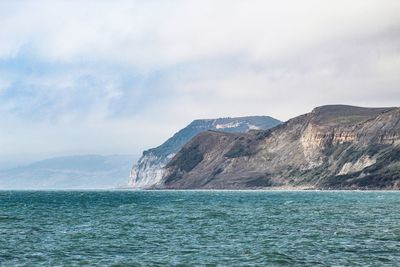 Scenic view of sea by mountain against sky