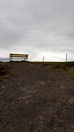 Empty bench on field against sky