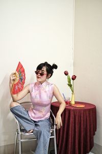 Portrait of woman in pink cheongsam top and jeans holding a fan