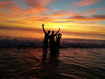 Silhouette people standing at beach against sky during sunset